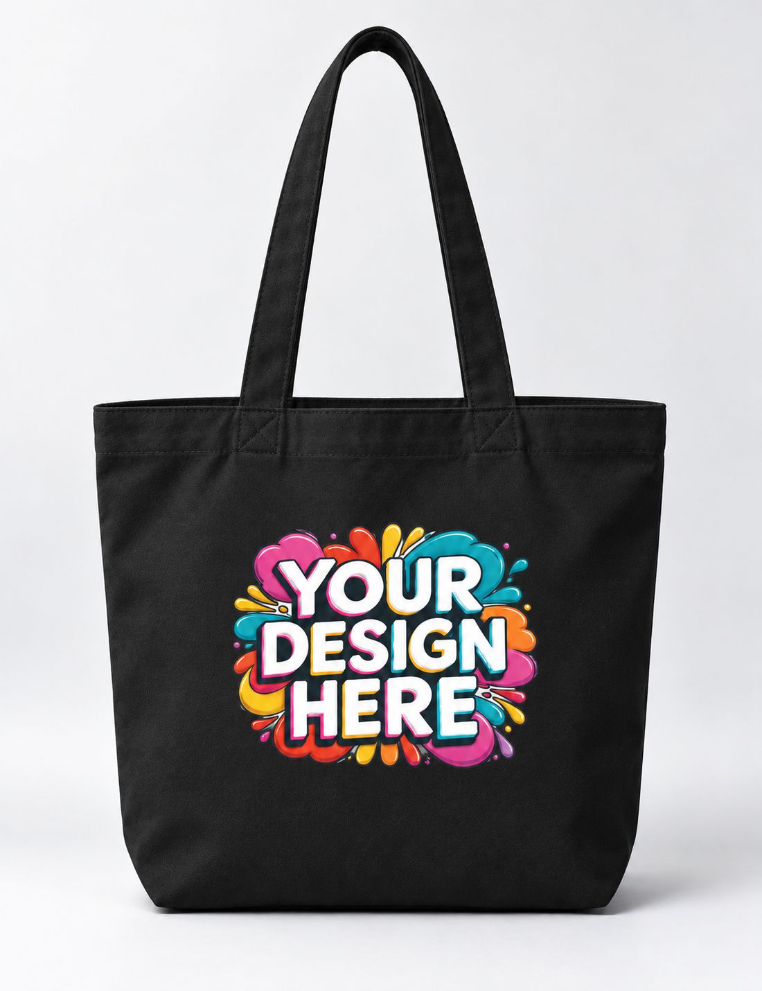 A black canvas tote bag with dual shoulder straps, featuring a colorful graphic print on the front that reads 'YOUR DESIGN HERE' in white letters over a vibrant paint splatter background.