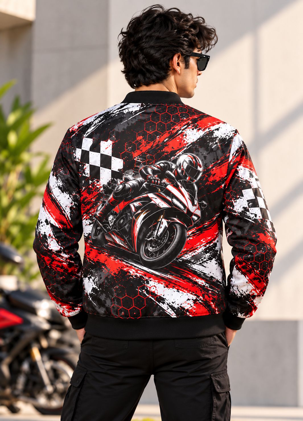 A man viewed from behind wearing a black bomber jacket with a large graphic print of a motorcycle racer on the back, featuring red and white brushstroke patterns and checkered flags.