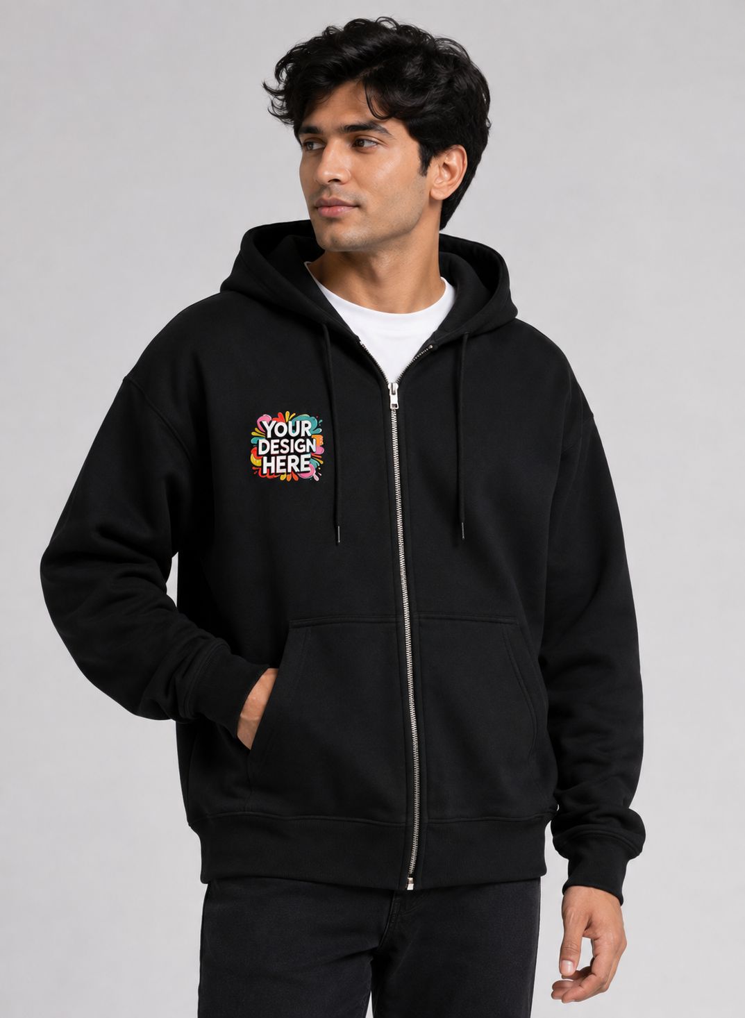 A man wearing a black zip-up hoodie with a colorful 'YOUR DESIGN HERE' mockup graphic on the left chest, photographed against a neutral gray studio background.