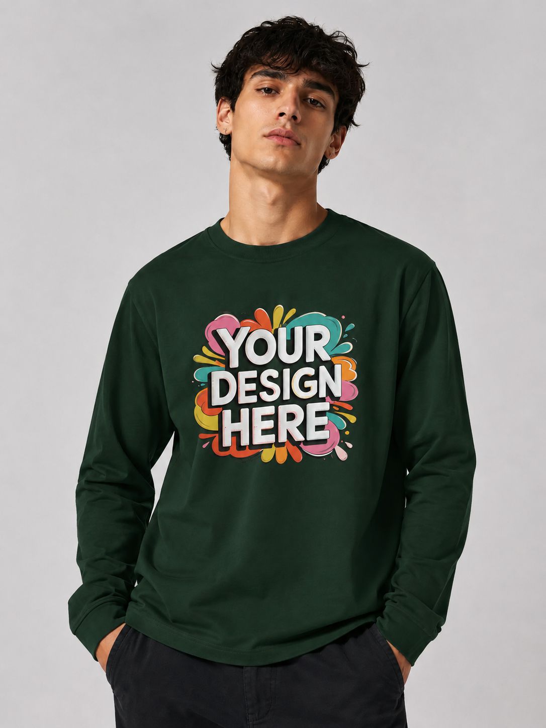 A man wearing a dark green long-sleeve crewneck sweatshirt with a colorful 'YOUR DESIGN HERE' mockup graphic on the chest, set against a plain light gray studio background.