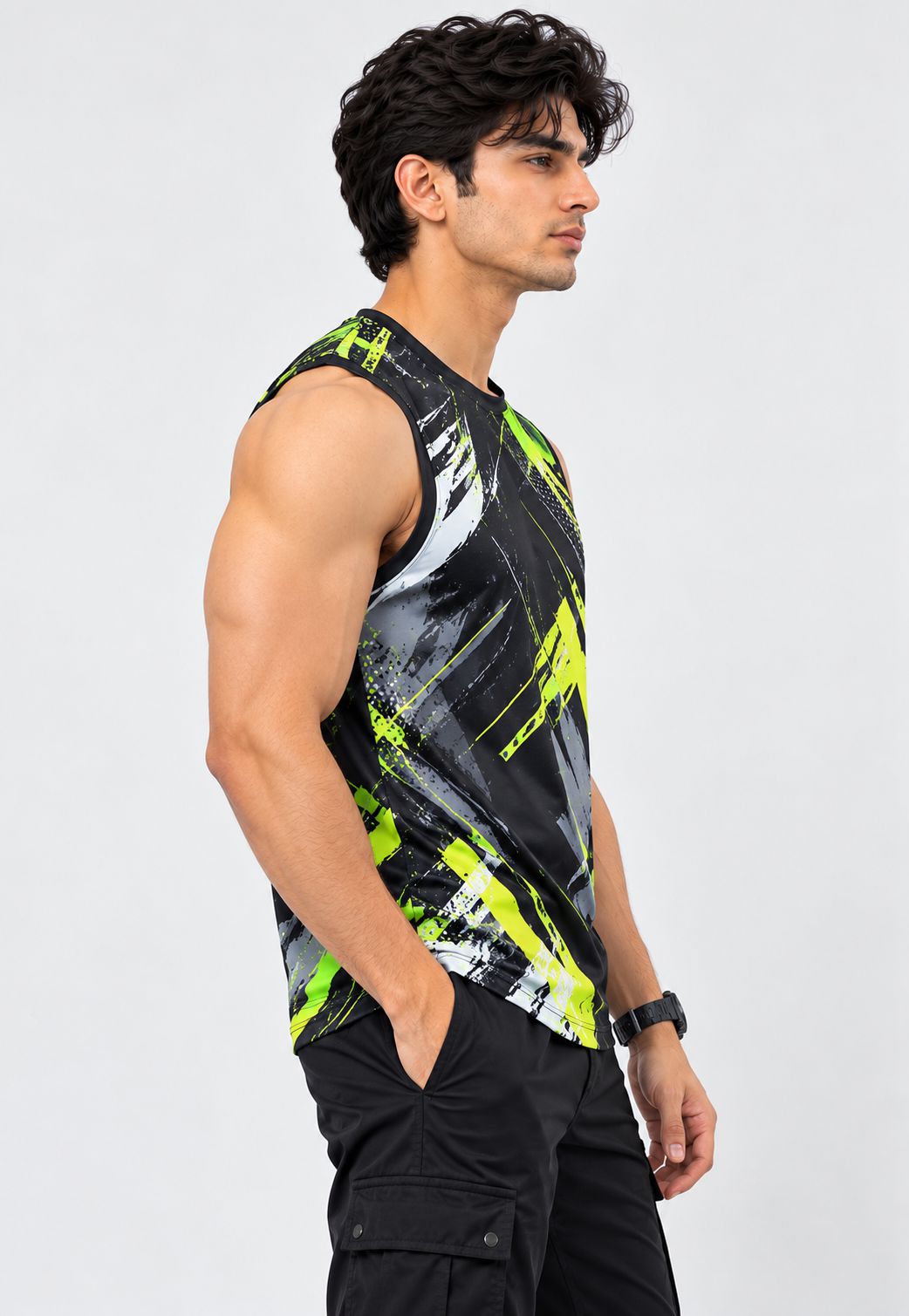 A man wearing a sleeveless athletic tank top with a black, gray, and neon yellow-green abstract brushstroke pattern, paired with black cargo pants, photographed against a light gray studio background.