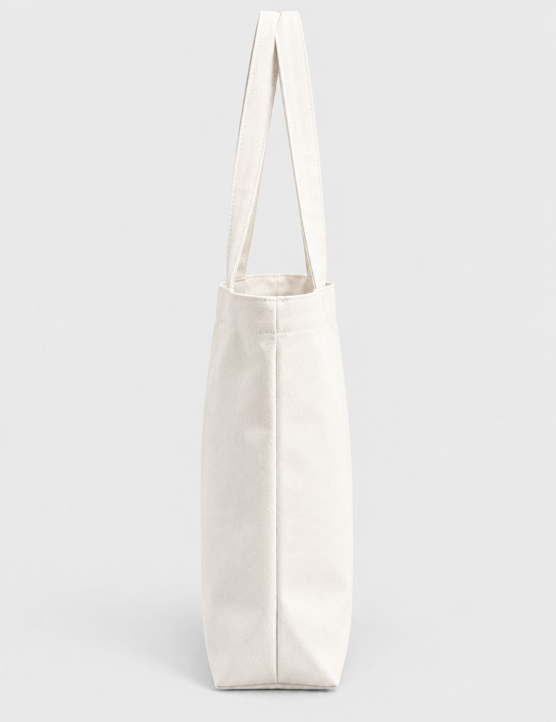 A plain off-white canvas tote bag with long shoulder straps, shown upright against a light gray studio background.