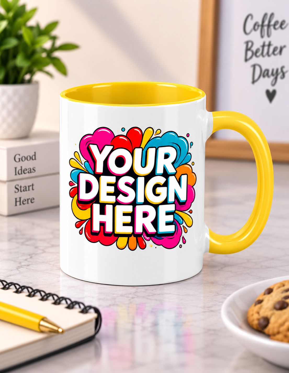 A white ceramic coffee mug with a bright yellow handle and interior, featuring a colorful abstract heart design with the text 'YOUR DESIGN HERE' in white. The mug is set on a marble desk with a notebook, plant, and cookie in a lifestyle setting.