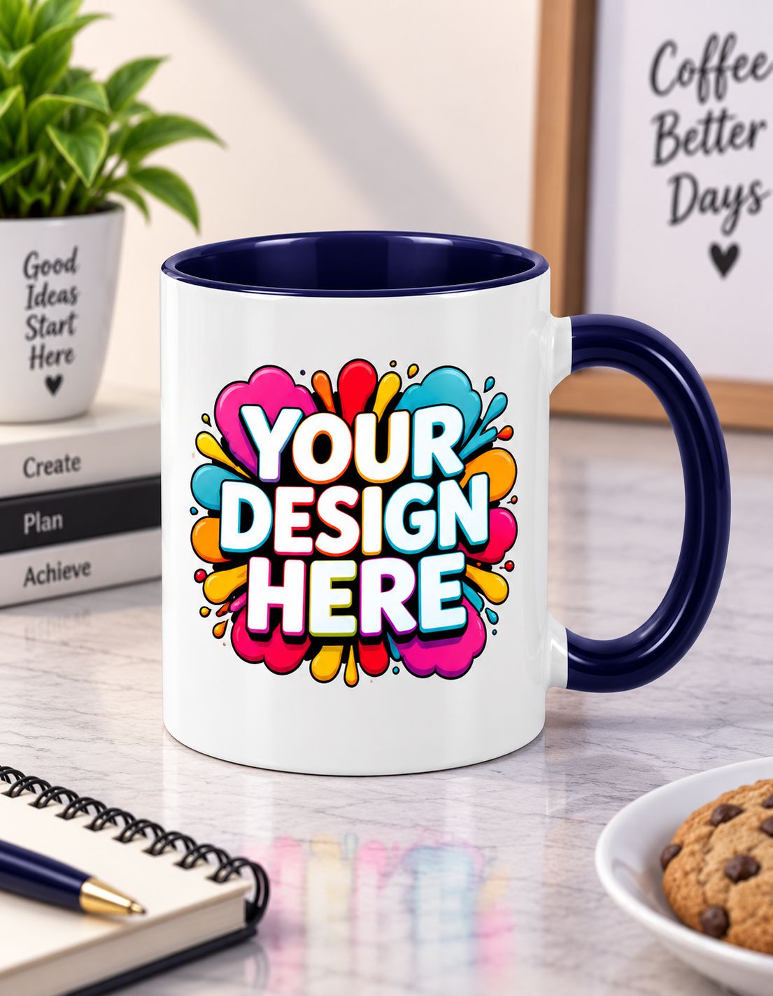A white ceramic coffee mug with a navy blue handle and interior, featuring a colorful 'YOUR DESIGN HERE' placeholder graphic on the front. The mug is set on a marble desk with a notebook, cookie, and a potted plant in the background.
