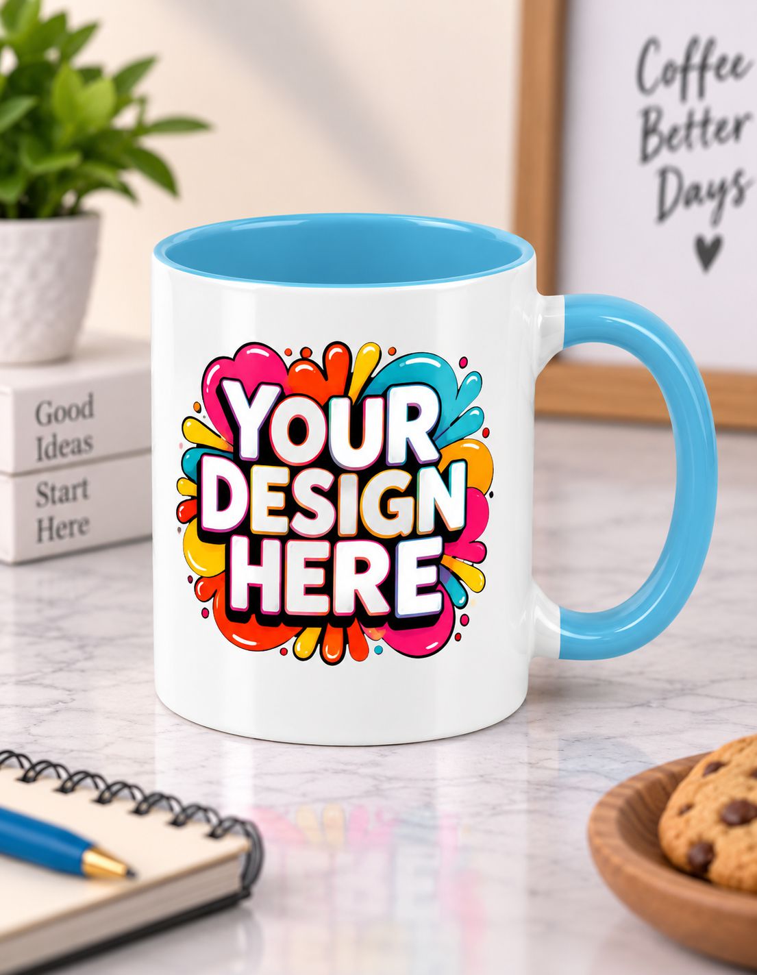A white ceramic mug with a bright blue handle and interior, featuring a colorful 'YOUR DESIGN HERE' placeholder graphic on the front. The mug is styled on a marble desk with a notebook, plant, and cookies in the background.