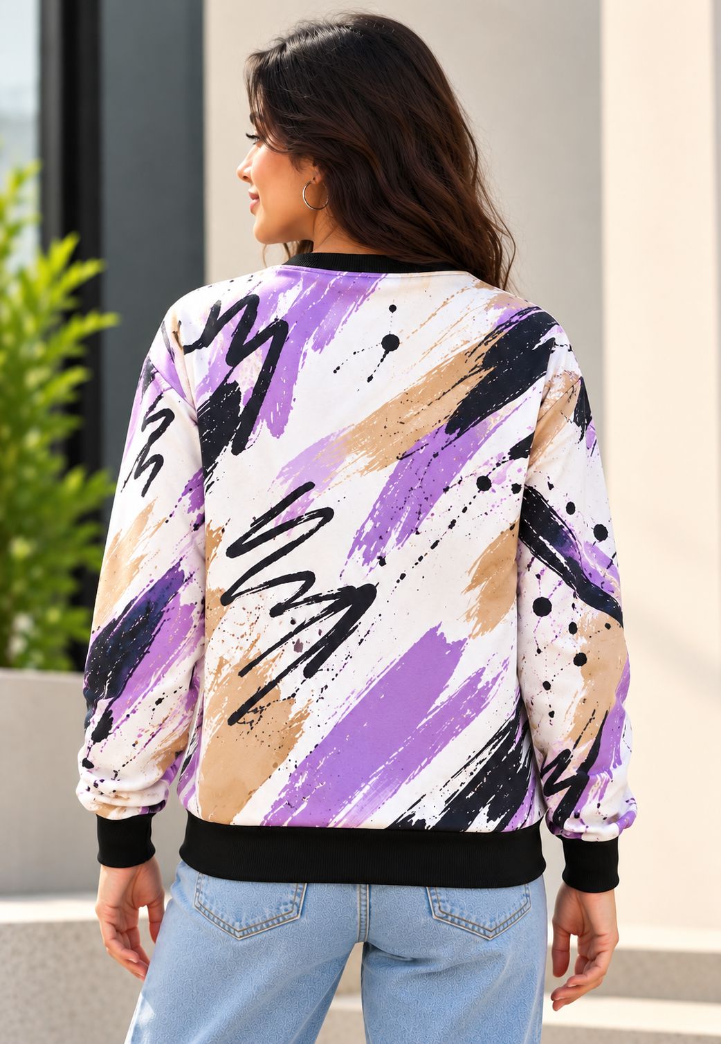 A woman shown from the back wearing a long-sleeve crewneck sweatshirt with an abstract paint stroke pattern in purple, beige, black, and white, paired with light blue jeans.