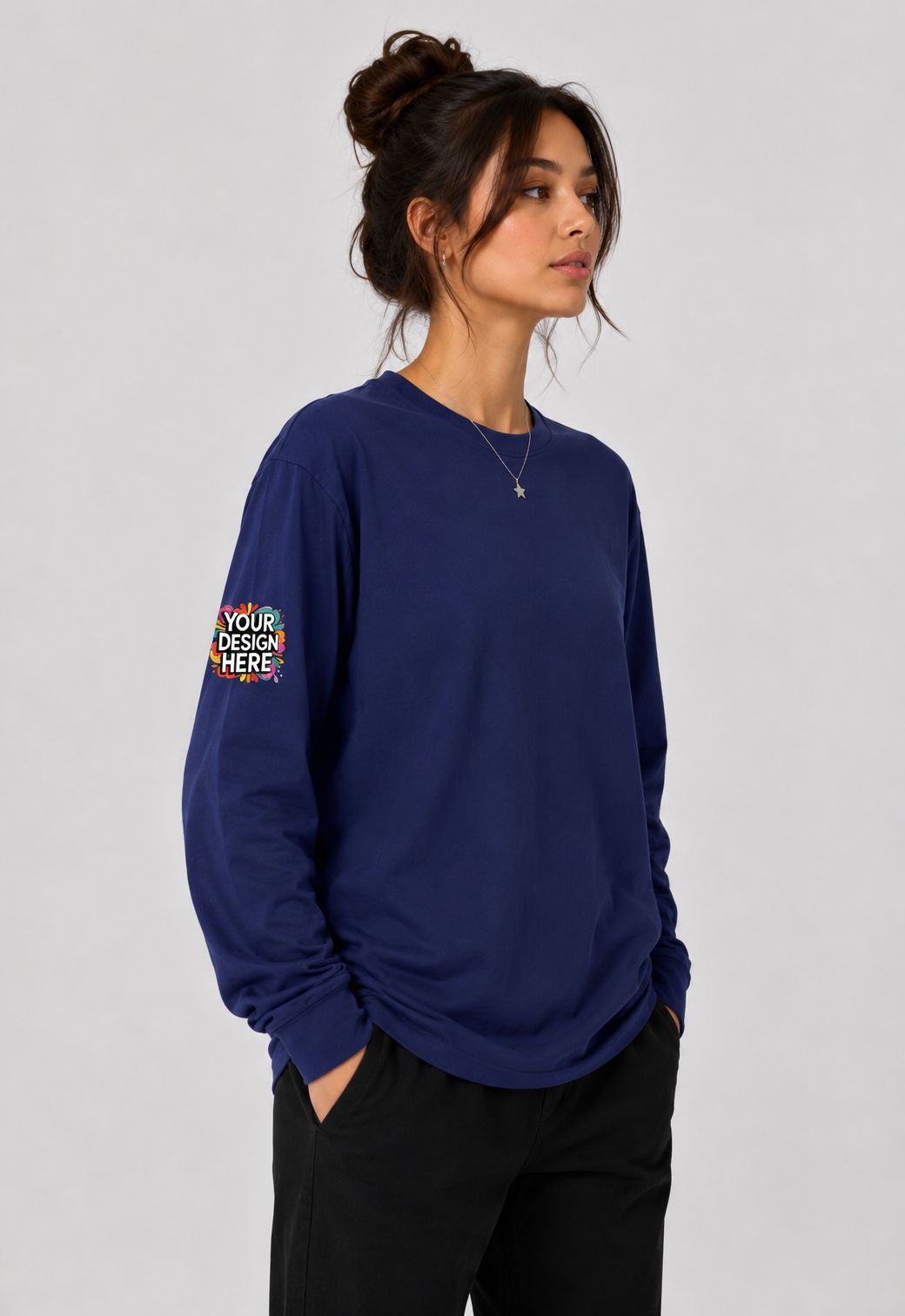 A woman wearing a navy blue long-sleeve crewneck sweatshirt with a colorful graphic print on the left sleeve, paired with black pants, against a light gray studio background.