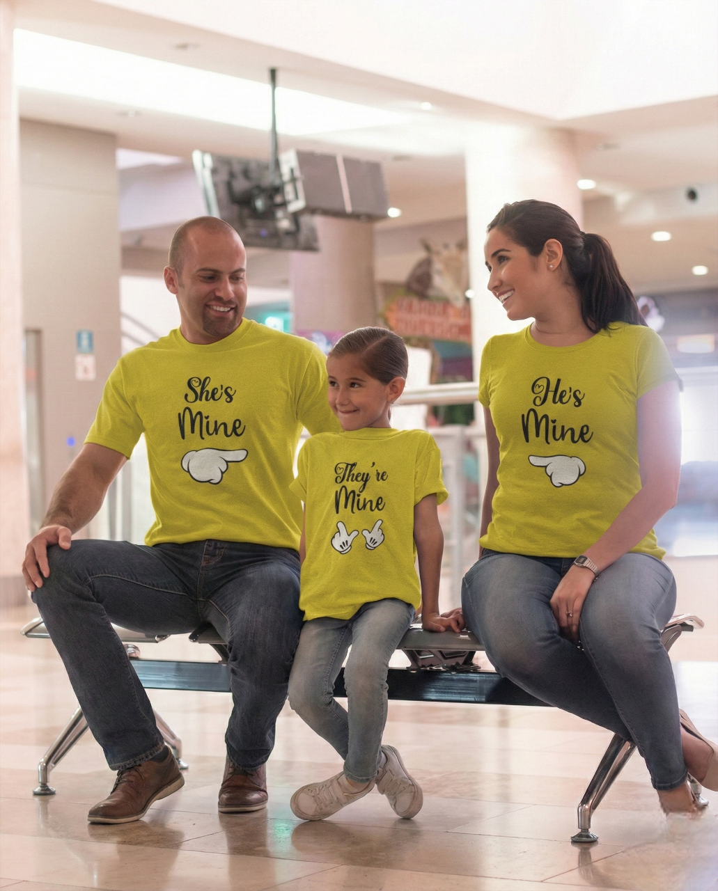 Family of three wearing matching yellow shirts with text in a shopping mall.