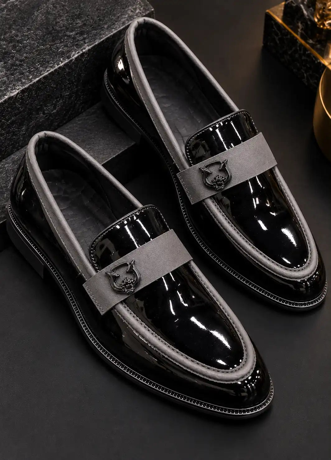Pair of black patent loafers with gray piping and emblem straps, viewed from above