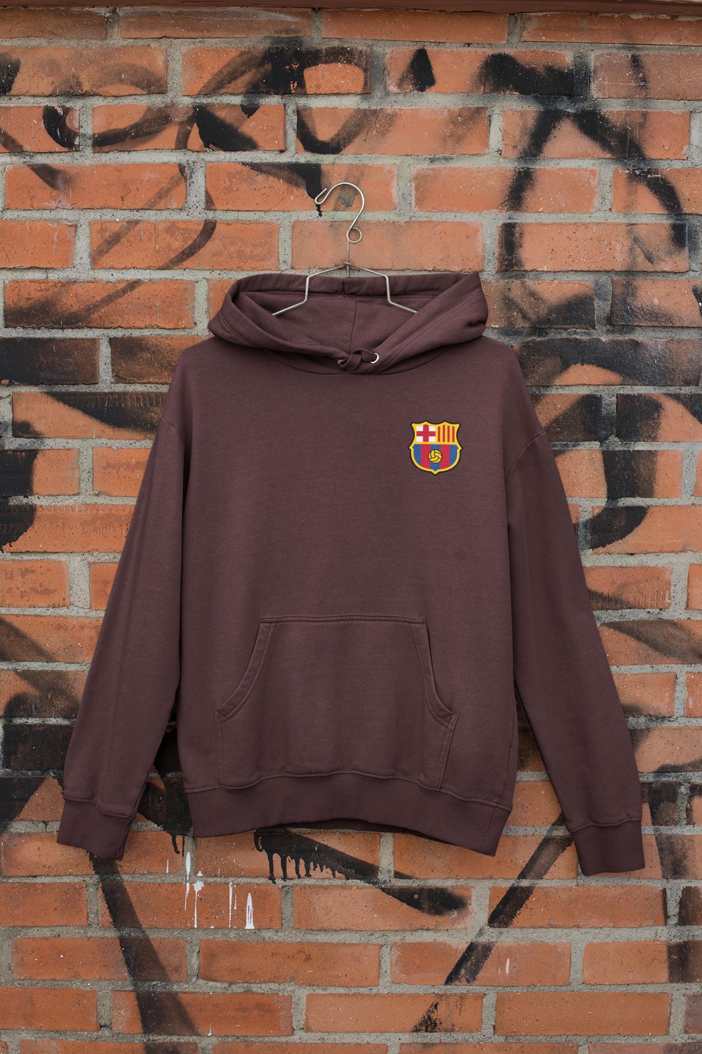 Maroon hoodie with a logo on a brick wall with graffiti