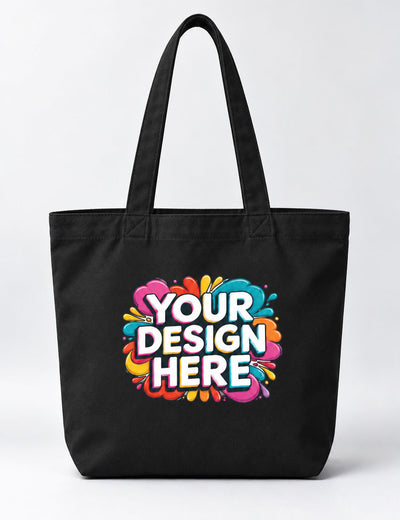 A black canvas tote bag with dual shoulder straps, featuring a colorful graphic print on the front that reads 'YOUR DESIGN HERE' in white letters over a vibrant paint splatter background.