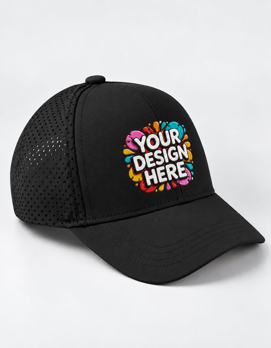 A black trucker-style sports cap with a curved brim and perforated mesh back panels, featuring a colorful graphic on the front that reads 'YOUR DESIGN HERE' in white text over a pink, blue, yellow, and orange paint splatter design. The cap is photographed on a clean white background.
