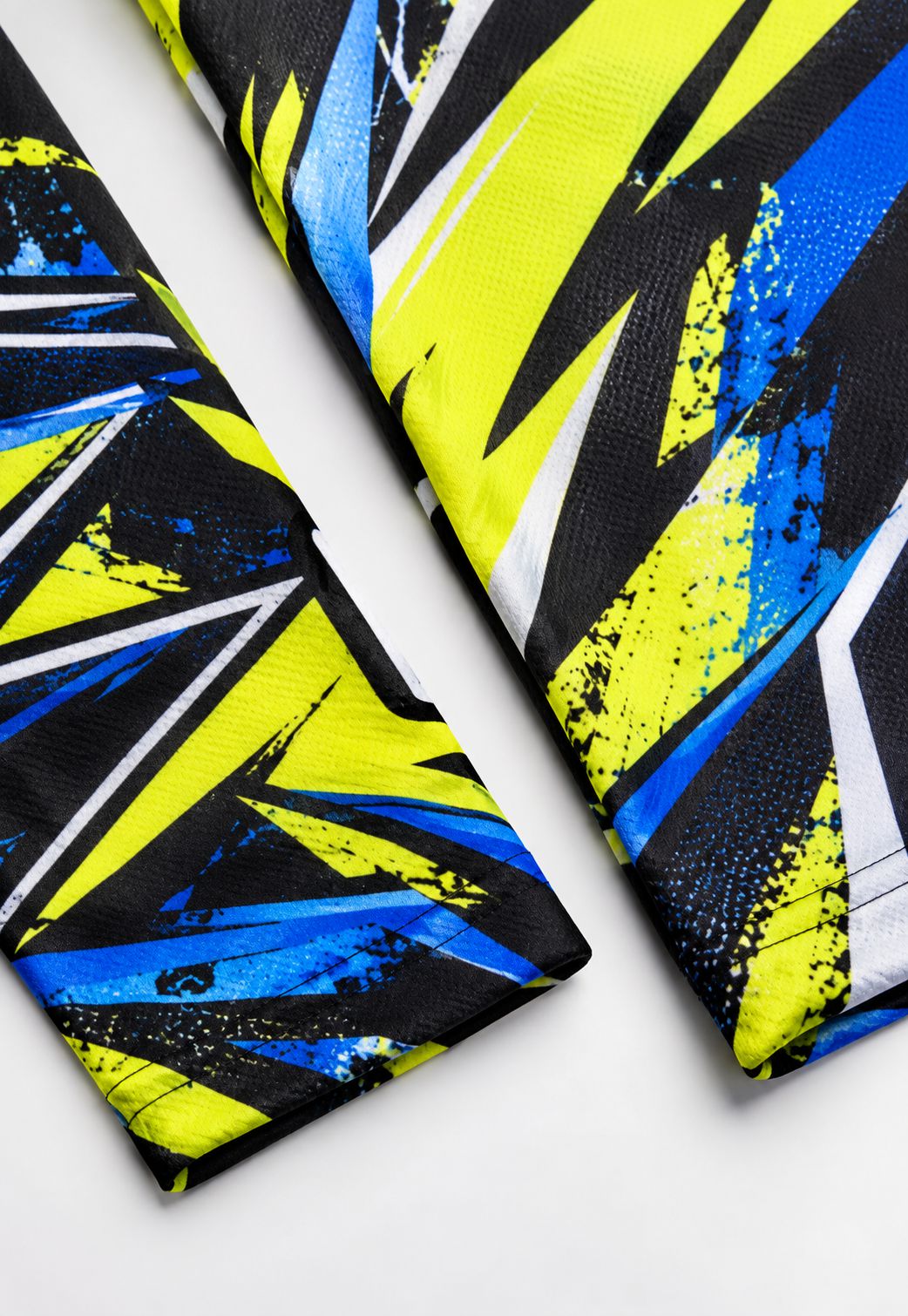 A close-up of a folded necktie featuring a bold abstract geometric pattern in neon yellow, blue, black, and white on a light gray background.