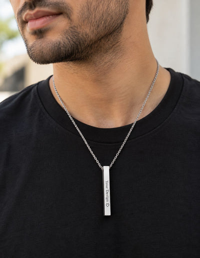 A close-up of a man wearing a silver bar necklace with custom engraving on a black t-shirt.