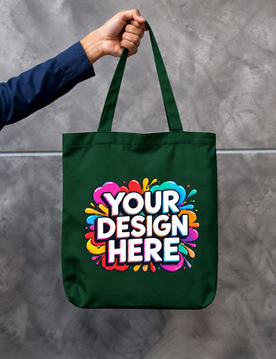 A dark green canvas tote bag with a colorful 'YOUR DESIGN HERE' mockup graphic, held by a person's hand against a gray concrete wall.