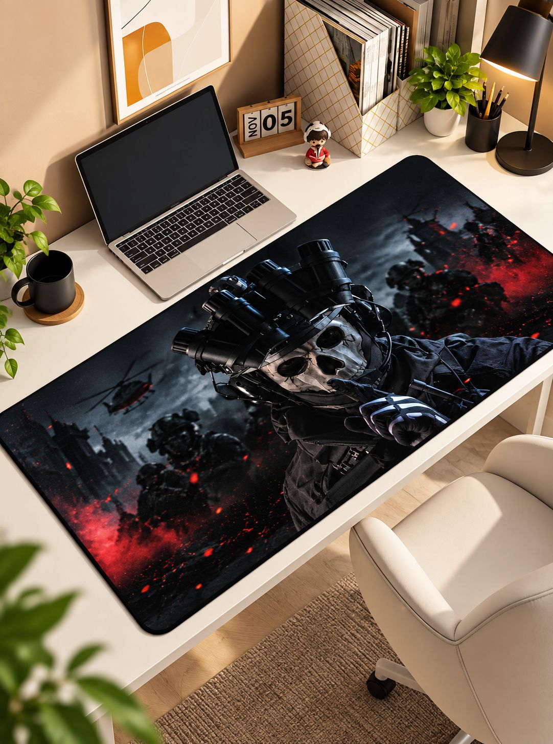 A large rectangular desk mat with a dark sci-fi graphic of a skull and robotic hand, shown on a white desk in a styled home office setup with a laptop, lamp, plants, and chair.