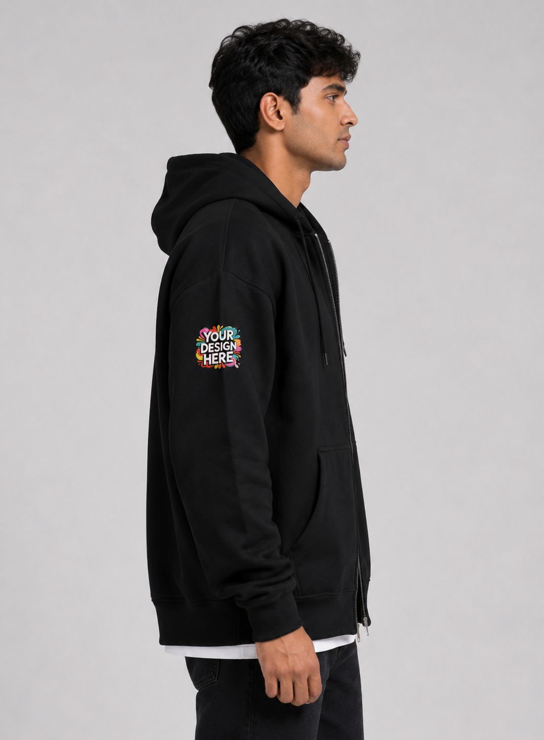 A man in profile wearing a black zip-up hoodie with a colorful 'YOUR DESIGN HERE!' mockup graphic on the left sleeve, photographed against a neutral gray background.