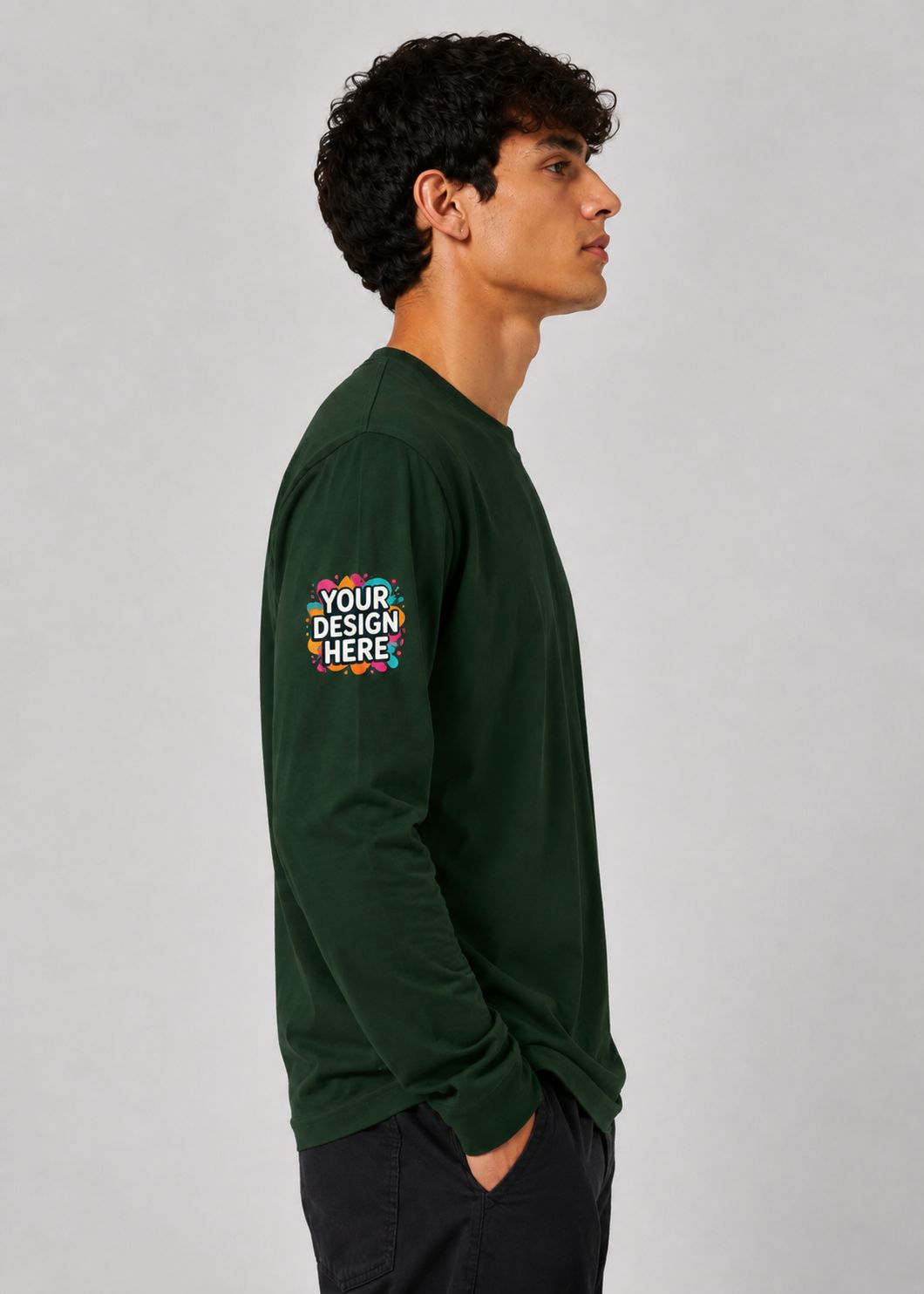 A man in profile wearing a dark green long-sleeve t-shirt with a colorful mockup graphic on the left sleeve that reads 'YOUR DESIGN HERE', set against a plain light gray background.