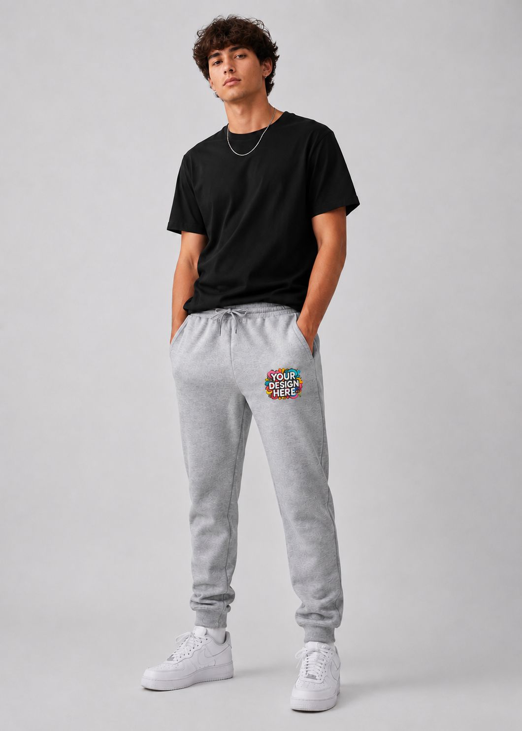 A man modeling a black crewneck t-shirt and light gray sweatpants with a colorful 'YOUR DOCTOR NAME HERE' graphic on the left thigh, paired with white sneakers, against a light gray studio background.