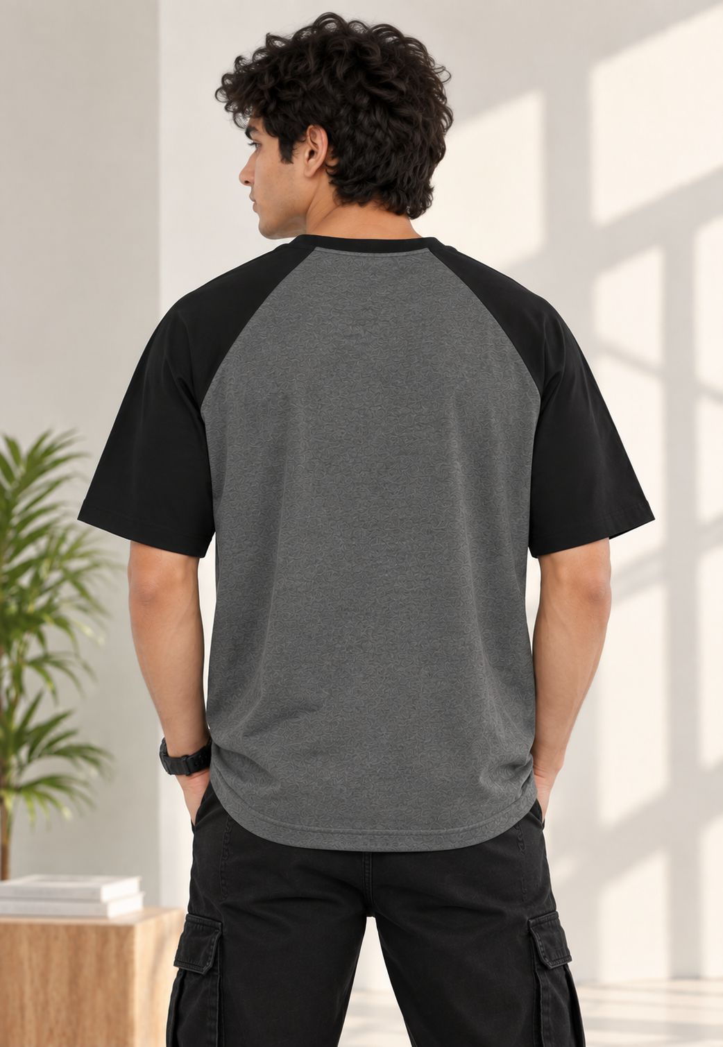 A man shown from the back wearing a short-sleeve raglan baseball t-shirt with a heather gray body and black sleeves, paired with black cargo pants in a bright indoor setting.