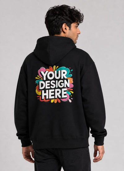 A man viewed from the back wearing a black hoodie with a colorful 'YOUR DESIGN HERE' mockup graphic printed on the back, set against a plain light gray studio background.