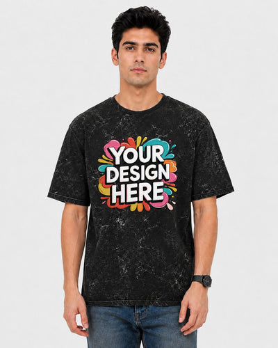 A man wearing a black mineral-wash t-shirt with a colorful 'YOUR DESIGN HERE' mockup graphic on the chest, paired with blue jeans, against a light gray background.