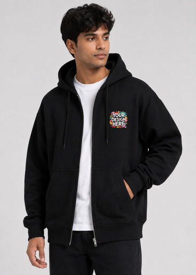 A man wearing a black zip-up hoodie with a colorful 'YOUR DESIGN HERE' mockup graphic on the left chest, layered over a white t-shirt and black pants, against a light gray studio background.