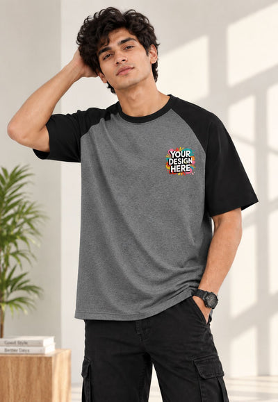 A man wearing a gray and black raglan t-shirt with a colorful 'YOUR DESIGN HERE' mockup graphic on the left chest, paired with black cargo pants in a bright indoor setting.