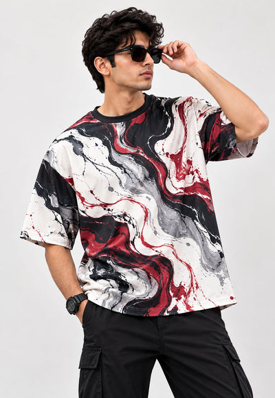 A man wearing a short-sleeve crewneck t-shirt with a black, white, and red marble swirl pattern, paired with black cargo pants and sunglasses, against a light gray studio background.