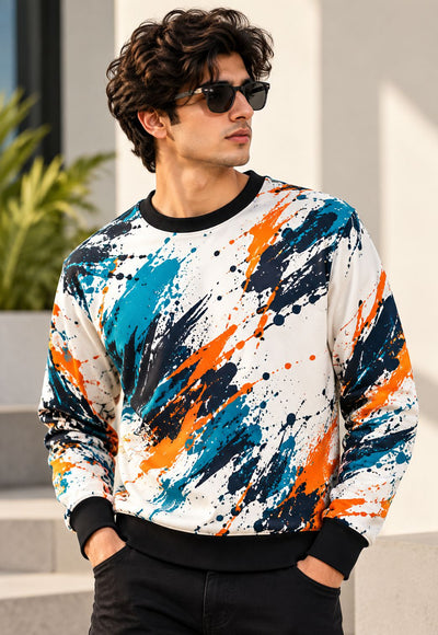 A man wearing a white crewneck sweatshirt with a vibrant blue, orange, and navy paint splatter pattern, styled with black pants and sunglasses.
