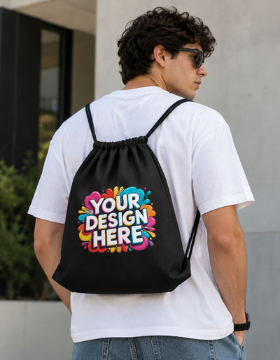 A man wearing a white t-shirt and sunglasses, shown from behind to display a black drawstring backpack with a colorful 'YOUR DESIGN HERE' graphic on the back.