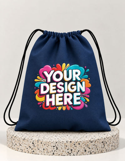 A navy blue drawstring bag with black cords, featuring a colorful 'YOUR DESIGN HERE' graphic on the front, displayed on a round speckled stone pedestal against a light gray background.