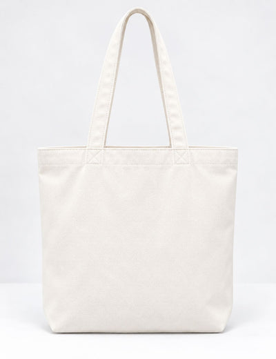 A plain canvas tote bag in off-white with dual shoulder straps, photographed against a seamless white studio background.