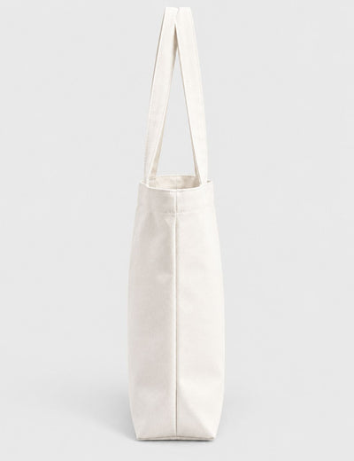 A plain off-white canvas tote bag with long shoulder straps, shown upright against a light gray studio background.
