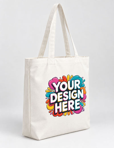 A white canvas tote bag with dual shoulder straps, featuring a colorful 'YOUR DESIGN HERE' mockup graphic on the front, set against a plain light gray studio background.