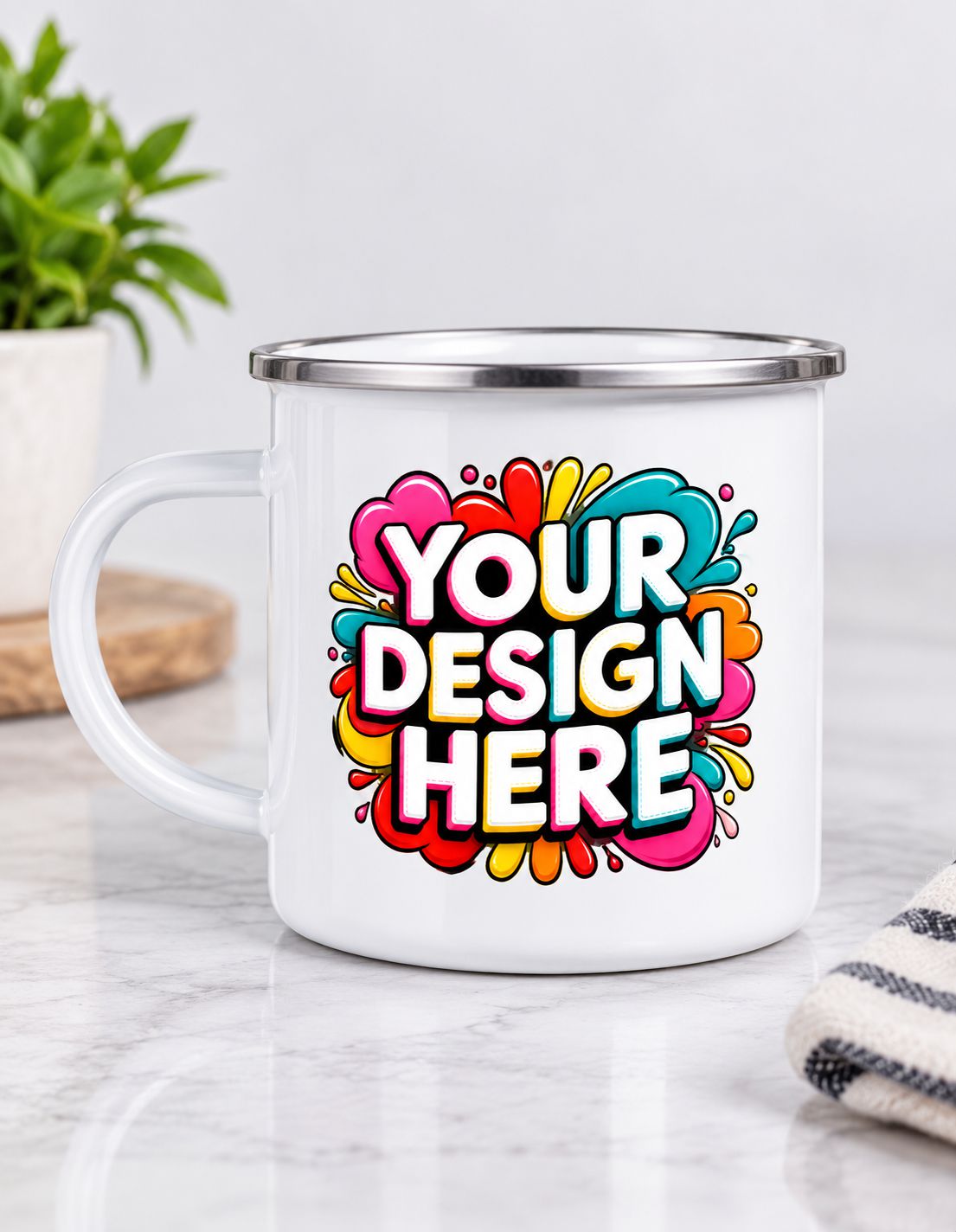 A white enamel-style mug with a silver metal rim sits on a light marble surface. The mug features a colorful printed graphic with the words 'YOUR DESIGN HERE' in bold white letters over a bright multicolor abstract splash design.