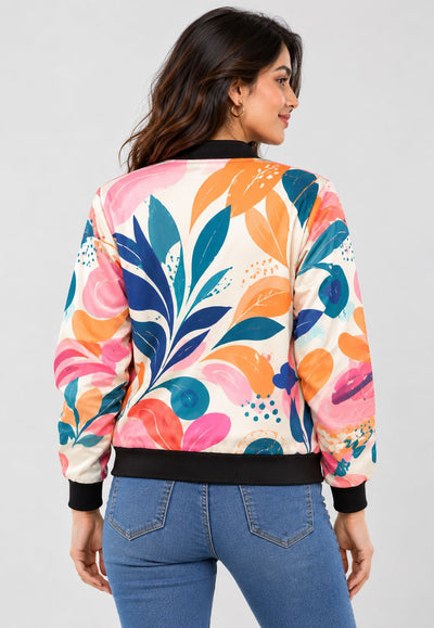 A woman shown from the back wearing a long-sleeve bomber jacket with a colorful abstract floral pattern in pink, orange, teal, and blue on a cream background, paired with blue jeans against a light gray studio background.