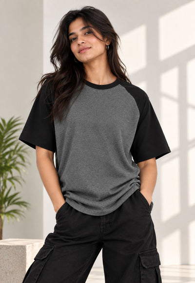 A woman wearing a heather gray and black raglan t-shirt with black cargo pants, standing in a brightly lit room with window shadows.