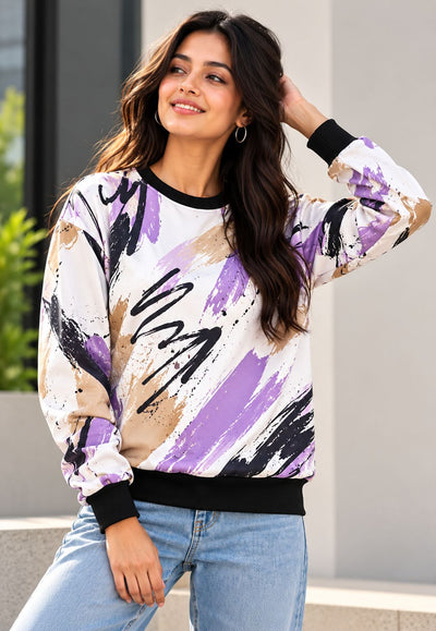 A woman wearing a long-sleeve crewneck sweatshirt with an abstract brushstroke pattern in purple, black, and beige on a white background, paired with light blue jeans.