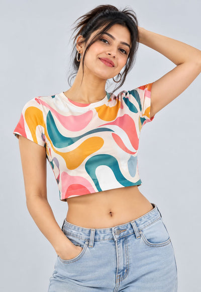 A woman wearing a short-sleeve crop top with a colorful abstract wavy pattern in pink, orange, teal, and yellow on a white base, paired with light blue jeans, against a solid light gray background.