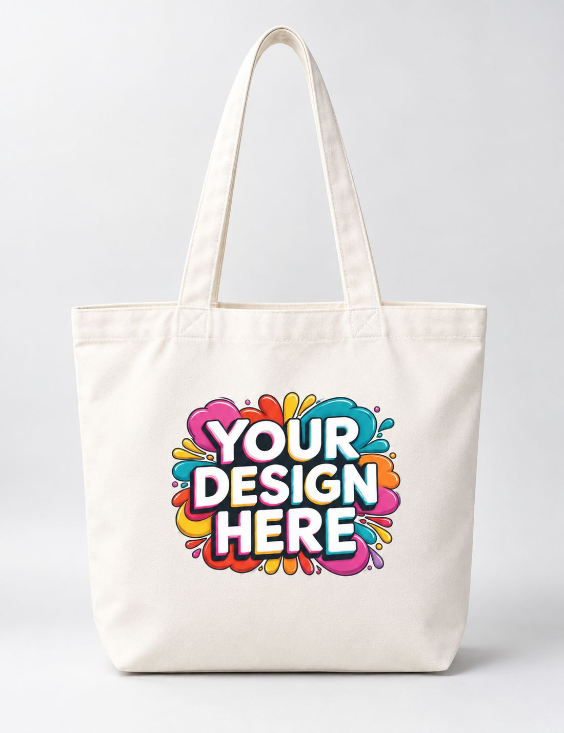 An off-white canvas tote bag with long handles, featuring a colorful 'YOUR DESIGN HERE' graphic printed on the front, set against a plain light gray background.