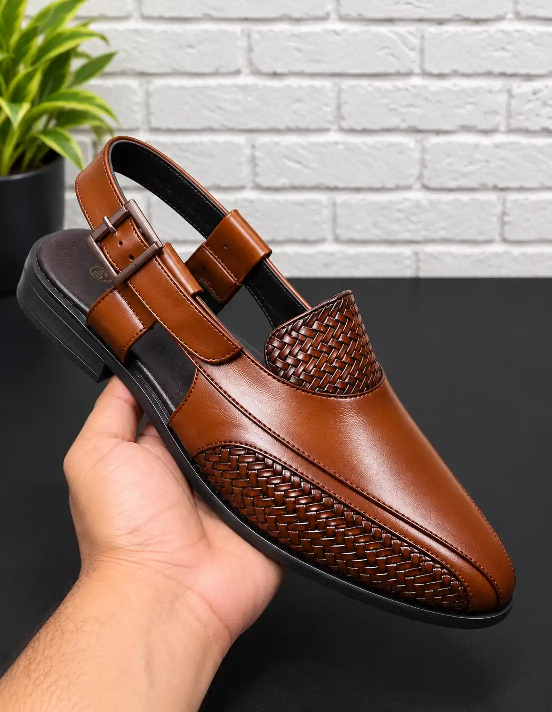 Tan men's Peshawari sandal held up, with woven panels, an open heel, and buckle strap