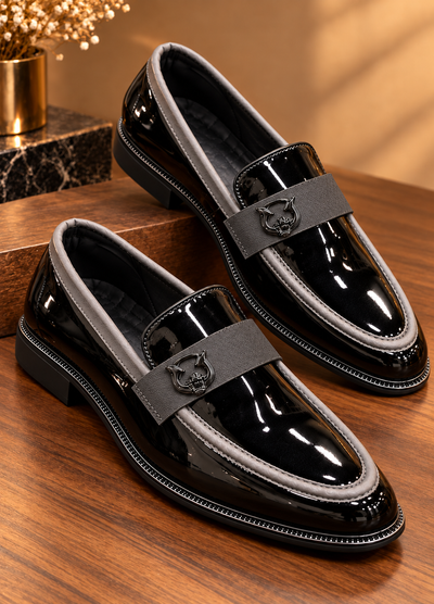Pair of black patent loafers with gray trim and emblem straps, angled view