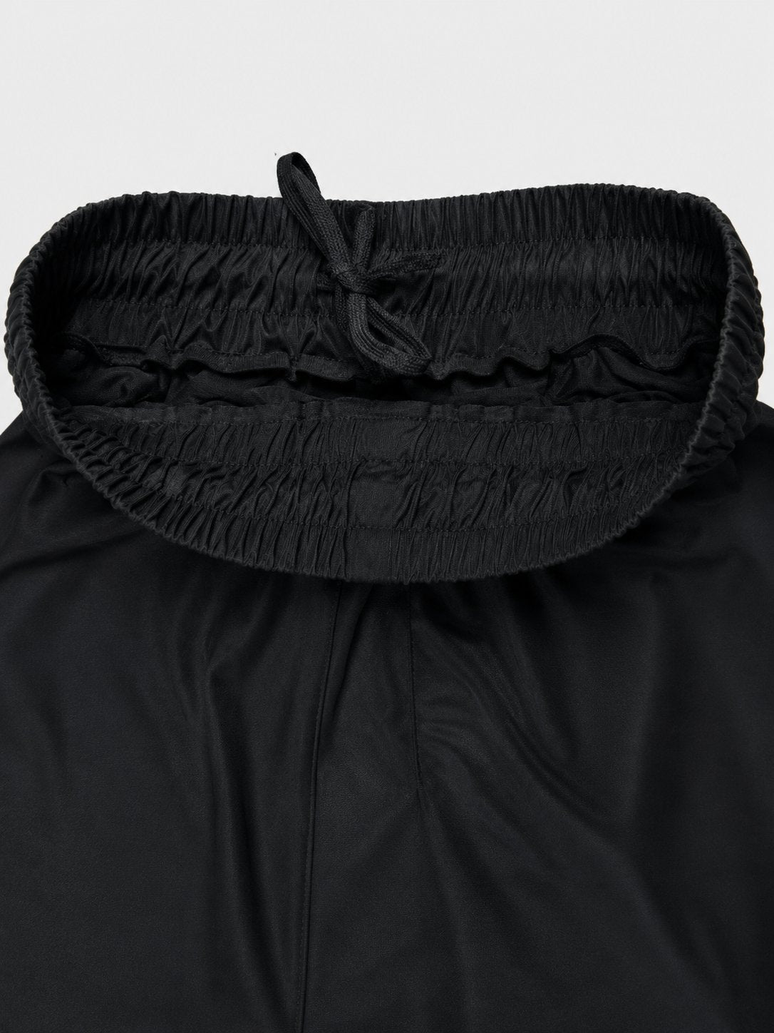 Close-up of a black garment with a wide, gathered elastic waistband and drawstring, shown against a light gray background.