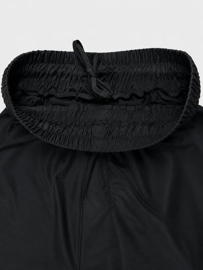 Close-up of a black garment with a wide, gathered elastic waistband and drawstring, shown against a light gray background.