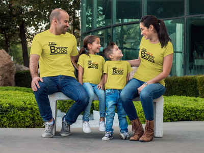 Family of four wearing matching yellow t-shirts with 'The Boss' text, sitting outdoors.