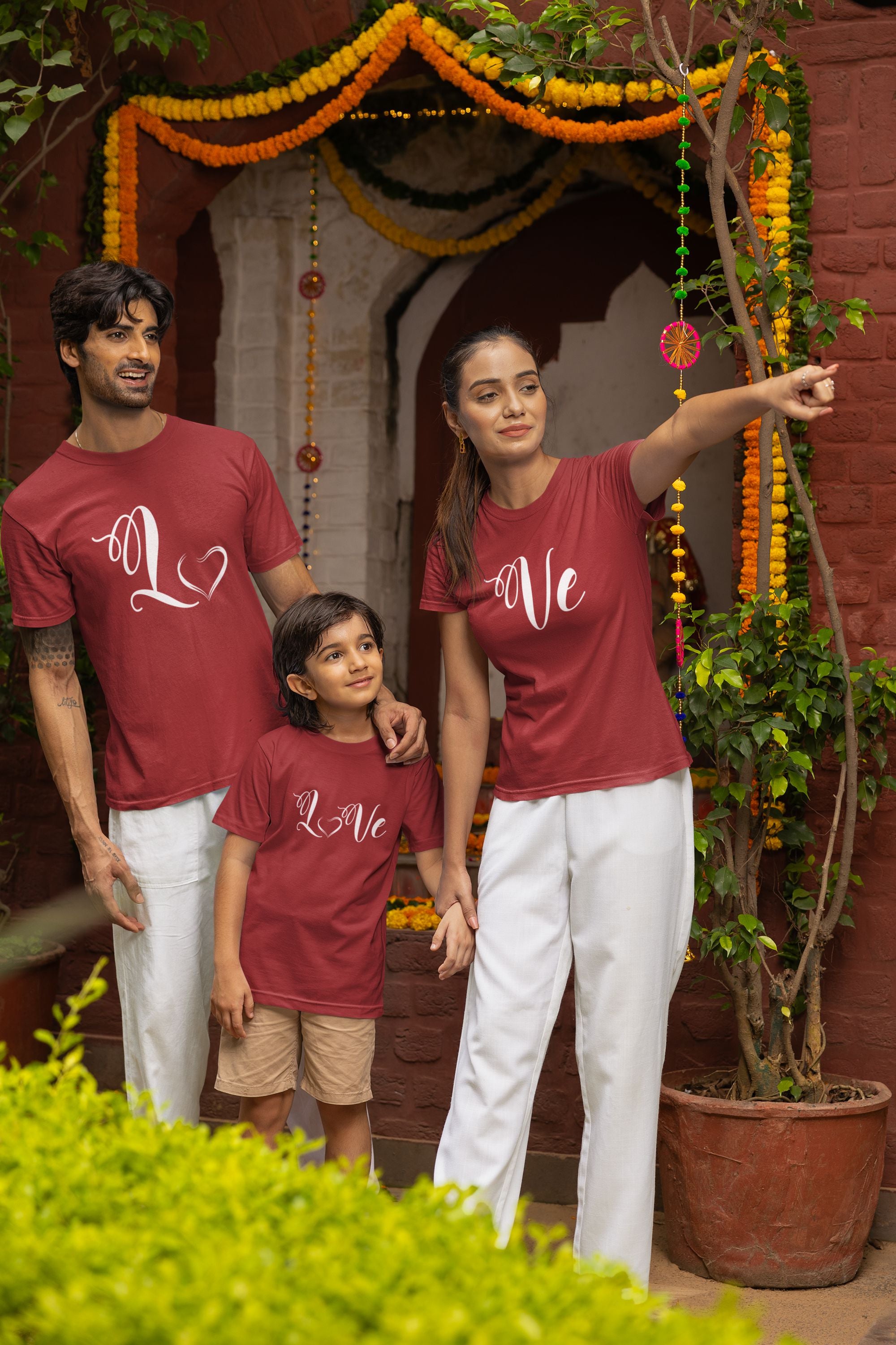 Family of three wearing matching red shirts with 'Love' printed on them, standing in front of a decorated entrance.