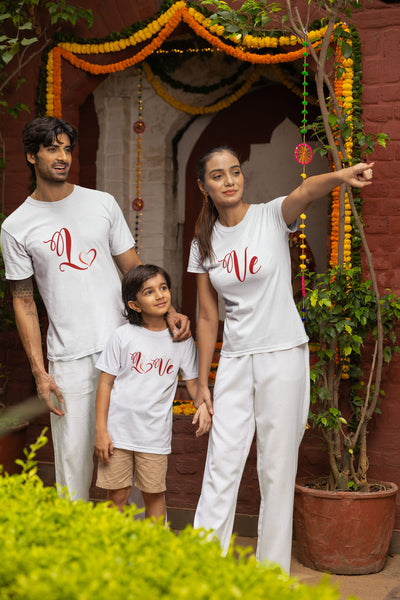 Family of three wearing matching white t-shirts with red text, standing in front of a decorated entrance.