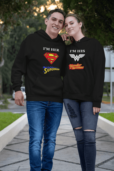 Man and woman wearing matching superhero-hemed hoodies on a sidewalk.