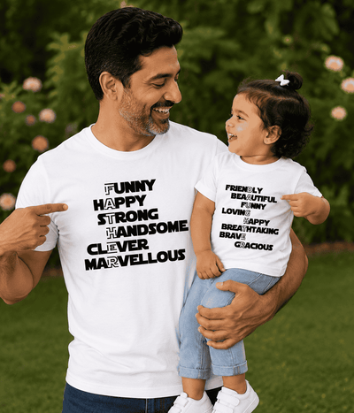 Man holding a child wearing matching white t-shirts with positive affirmations in an outdoor setting.